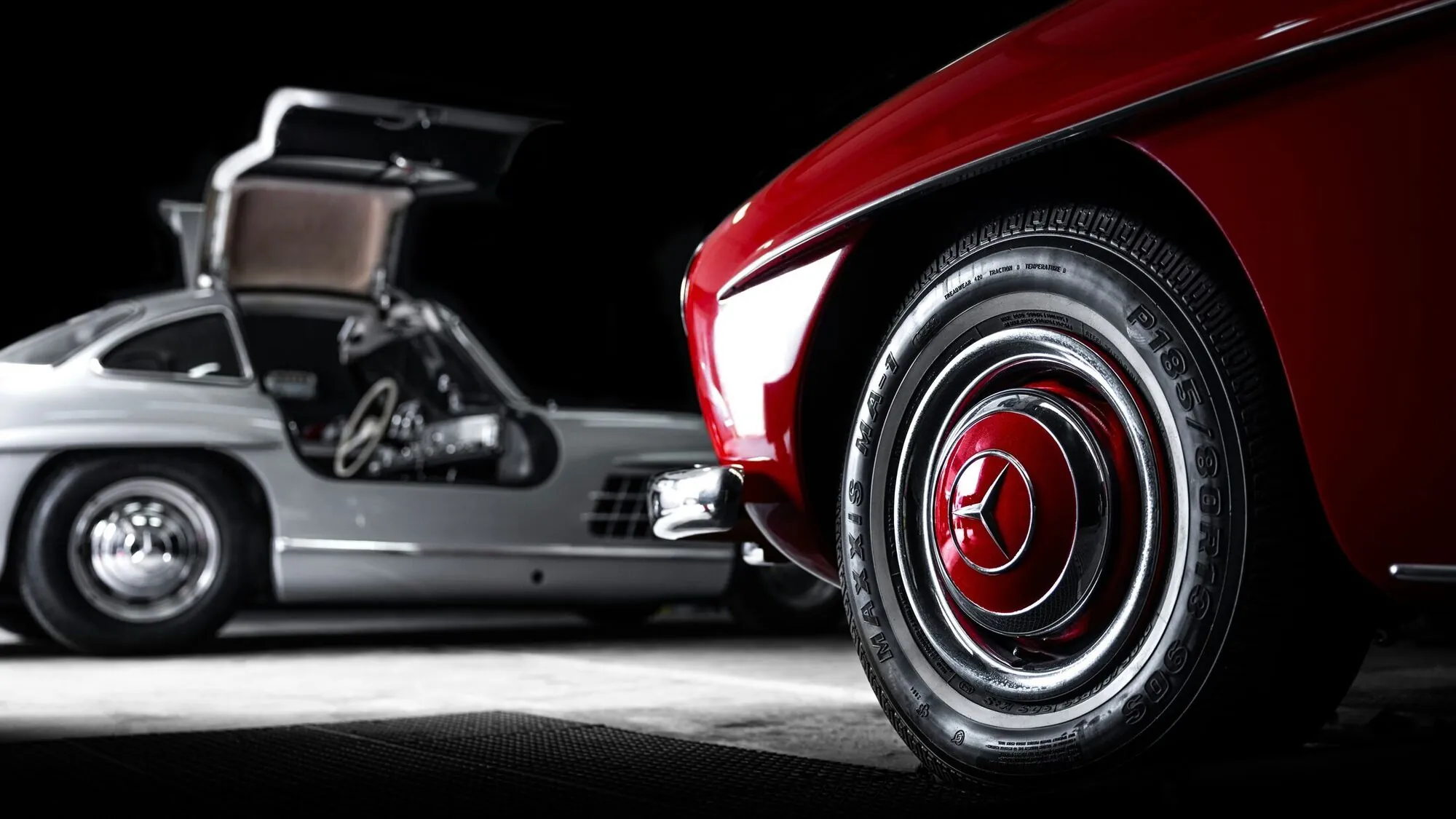 Two Mercedes-Benz 300 SL Gullwings under studio light, one silver with its door raised